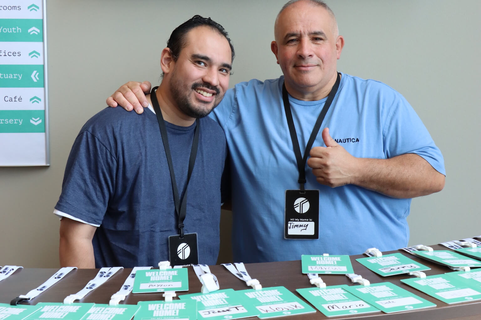 two men with arm wrapped around shoulder and thumbs up facing camera