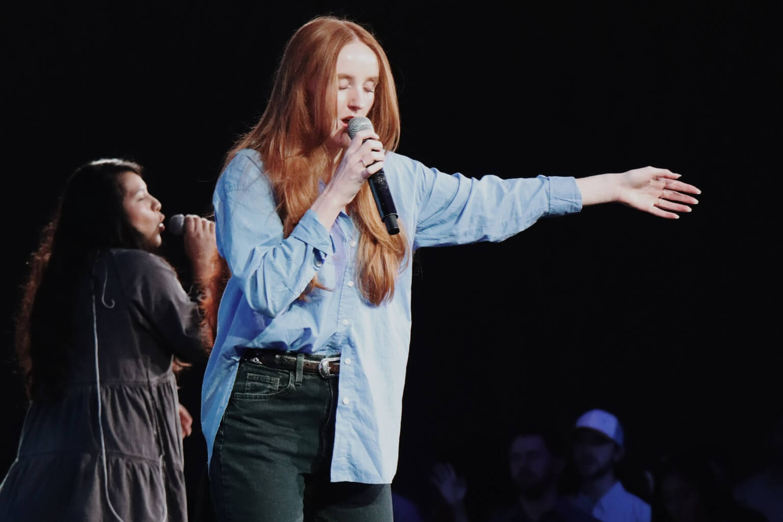 two women singing in front of stage